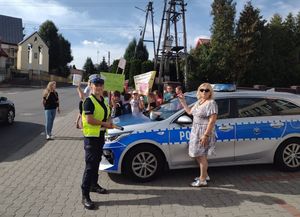 Policjanci z dziećmi z Wierzchalsa biorą udział w akcji Jabłko i Cytryna. Stoją przy radiowozie przy drodze.