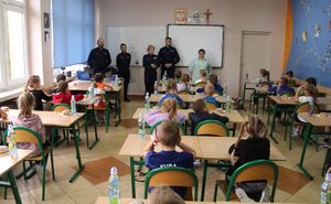 Uczniowie biorący udział w konkursie siedzą w ławkach w sali. Z przodu stoją policjanci oraz wicedyrektor Zespołu Szkół numer 1 w Wieluniu.