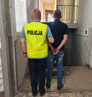 Policjant prowadzi zatrzymanego po korytarzu w budynku komendy policji.