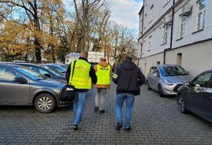 Policjanci z grupy dochodzeniowo śledczej idą wzdłuż budynku starostwa.