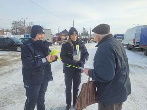 Policjantki rozdają napotkanym przechodniom elementy odblaskowe, ulotki.