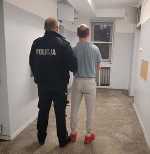 Policjant prowadzi zatrzymanego do pomieszczeń dla osób zatrzymanych.
