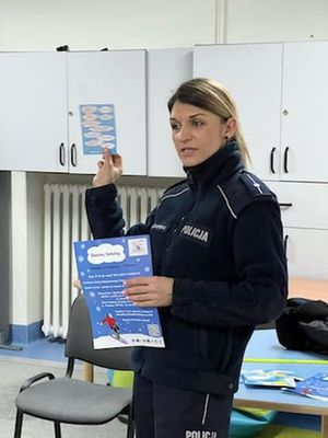 Policjantka prezentuje plakat dotyczący bezpiecznych zachowań podczas zabaw zimowych.