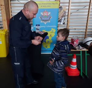 Policjant w ramach wystawionego stoiska profilaktyczno promocyjnego wystawionego w hali Zespołu Szkół numer 1 w Wieluniu rozmawia z chłopcem.