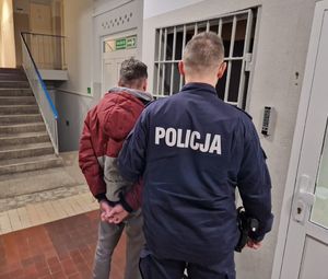 Policjant prowadzi zatrzymanego po korytarzu w budynku komendy policji.