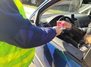 Policjant wręcza kierowcy siedzącemu w samochodzie serduszko zapachowe.