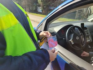 Policjant wręcza kierowcy siedzącemu w samochodzie serduszko zapachowe.