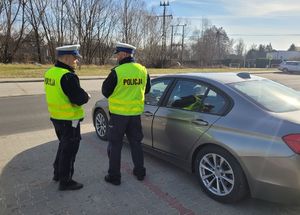 Policjanci stoją przy radiowozie nieoznakowanym i nadzorują ruch na drodze.