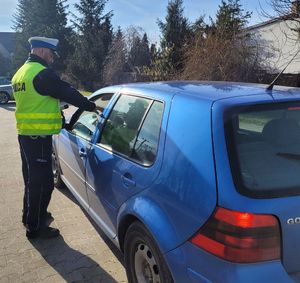 Policjant wręcza kierowcy siedzącemu w samochodzie serduszko zapachowe.