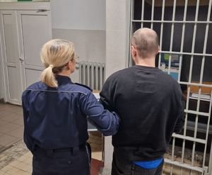 Policjantka prowadzi zatrzymanego po korytarzu w budynku komendy.