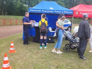 Policjant stoi przy stoisku, podchodzą do niego przechodnie.