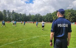 Drużyna policjantów rozgrywająca mecz na boisku. Z boku stoi umundurowany policjant.