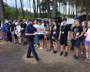 Policjant rozdaje ulotki dotyczące bezpiecznych zachowań  młodzieży wypoczywającej w Nadwarciańskim Grodzie.