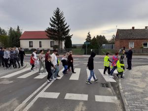 zdjęcie przedstawia policjanta przeprowadzającego dzieci i młodzież przez przejście dla pieszych