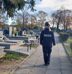 Policjantka idzie alejką przez cmentarz.