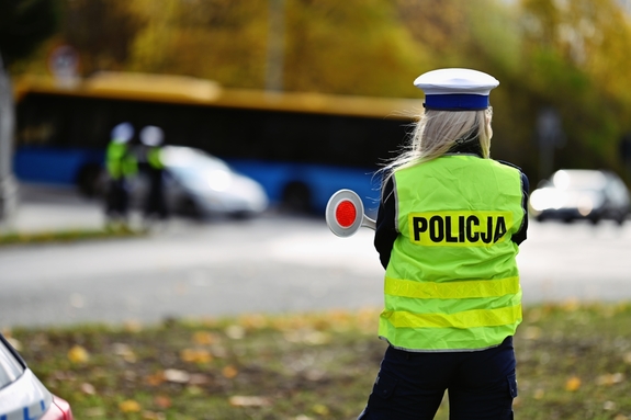 Policjantka stoi tyłem, trzyma w ręku tarczę do zatrzymywania.