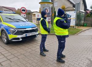 Policjantki stoją przy drodze, jedna mierzy prędkość z tyłu stoi radiowóz.