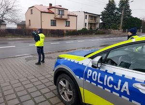 Radiowóz stoi na poboczu, policjantka używa miernika prędkości.