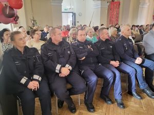 Policjanci i seniorzy siedzą na krzesłach w Wieluńskim Domu Kultury.