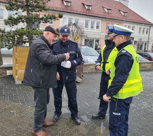 Policjanci wręczają przechodniom długopisy i elementy odblaskowe.