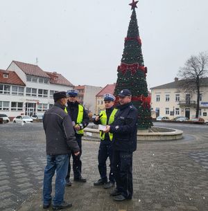 Policjanci wręczają przechodniom długopisy i elementy odblaskowe.