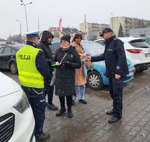 Policjanci wręczają przechodniom długopisy i elementy odblaskowe.