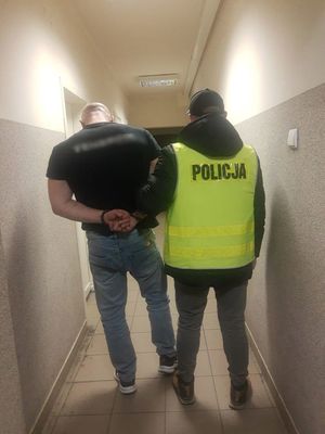 Policjant prowadzi zatrzymanego po korytarzu w budynku komendy.