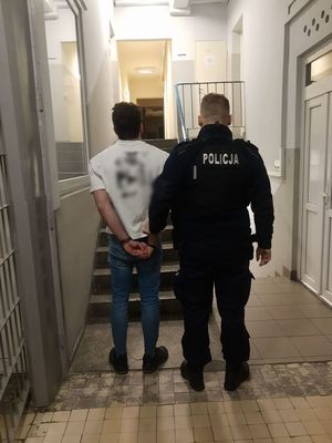 Policjant prowadzi zatrzymanego po korytarzu w budynku komendy.