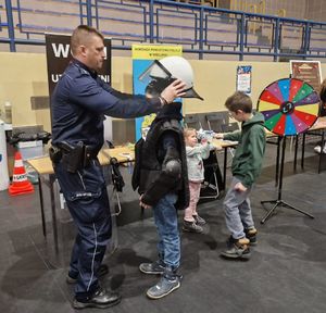 Policjant zakłada hełm policyjny dziecku na głowę.