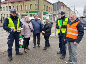 Policjanci wspólnie z przedstawicielem Przedsiębiorstwa Komunalnego na terenie miasta Wielunia rozdają opaski odblaskowe przechodniom.