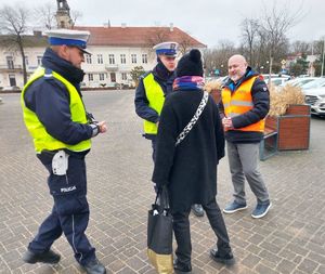 Policjanci wspólnie z przedstawicielem Przedsiębiorstwa Komunalnego na terenie miasta Wielunia rozdają opaski odblaskowe przechodniom.