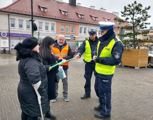 Policjanci wspólnie z przedstawicielem Przedsiębiorstwa Komunalnego na terenie miasta Wielunia rozdają opaski odblaskowe przechodniom.