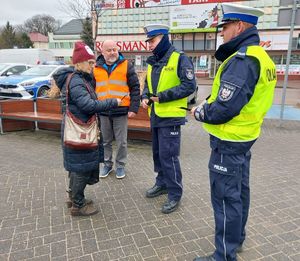 Policjanci wspólnie z przedstawicielem Przedsiębiorstwa Komunalnego na terenie miasta Wielunia rozdają opaski odblaskowe przechodniom.