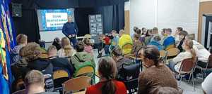 Policjant prowadzi pogadankę z uczniami w sali szkoły.