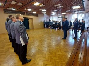 Aula w wieluńskiej jednostce Policji podczas uroczystej zbiórki. W dwuszeregu stoi kadra kierownicza, policjanci, policjantki pracownicy cywilni. Obok stoją zaproszeni goście, przedstawiciele władz samorządowych.. W sali obecny jest Komendant Powiatowy Policji w Wieluniu i jego I Zastępca. W szeregu stoją policjanci, którzy otrzymali rozkazy i wyróżnienia.