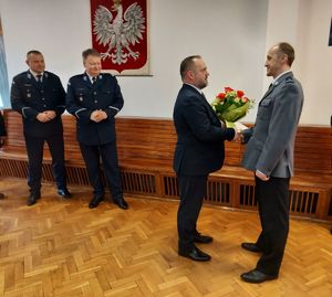 Starosta Wieluński wręcza kwiaty i podziękowania dla odchodzącego na emeryturę Komendanta Komisariatu Policji w Białej. W tle stoją komendanci policji.