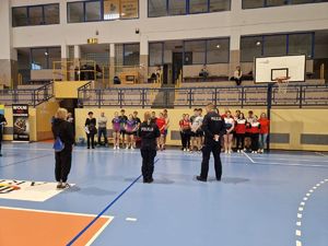 W hali sportowej stoją uczniowie wraz z nauczycielami na przeciwko stoją policjanci, którzy witają uczestników turnieju.