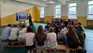 Policjantka w sali gimnastycznej z uczniami prowadzi pogadankę.