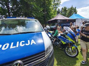 Policjanci na pikniku wystawili stoisko profilaktyczne, prezentują elementy umundurowania, prowadzą konkurs wiedzy o bezpieczeństwie dla najmłodszych. Z boku stoi radiowóz.