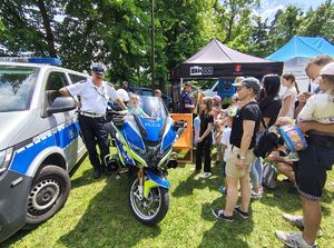 Stoisko profilaktyczne wystawione przez policjantów, z boku stoi radiowóz, policyjny motocykl.