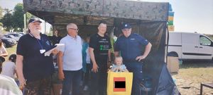 Policjant na pikniku profilaktycznym pozuje do zdjęcia z uczestnikami wydarzenia.