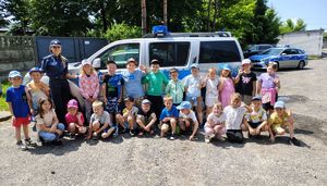 Policjanci wspólnie z dziećmi pozują do zdjęcia na tle radiowozu.