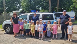 Policjanci wspólnie z dziećmi pozują do zdjęcia na tle radiowozu.