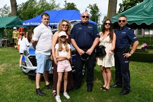 Policjanci na pikniku profilaktycznym pozują z uczestnikami do zdjęcia na tle radiowozu.