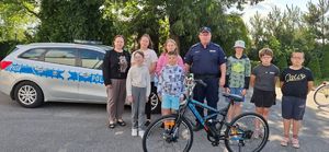 Policjanci na boisku szkolnym z dziećmi, w tle radiowóz.