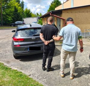 Policjant prowadzi zatrzymanego do auta.