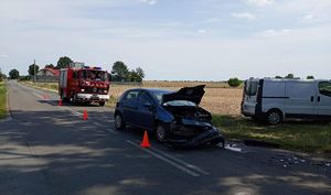 Uszkodzony samochód, który brał udział w zdarzeniu drogowym stoi na drodze. W oddali wóz strażacki.