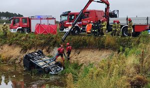 Miejsce zdarzenia, wozy strażackie. Auto wyciągane jest podnośnikiem ze stawu.