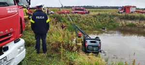 Miejsce zdarzenia, wozy strażackie. Auto wyciągane jest podnośnikiem ze stawu.