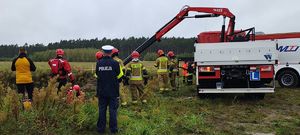 Wozy strażackie wokół stawu, strażacy , policjant zabezpiecza miejsce zdarzenia.